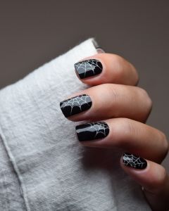 Hand mit UV Gel Wraps Spooky Days – tiefschwarze Nägel mit weißen Spinnennetzen, glänzendes Finish.