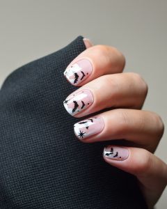 Hand mit Nailpolish Wraps Witch, Please – zarte French-Basis mit schwarzen Fledermäusen und Sternen.